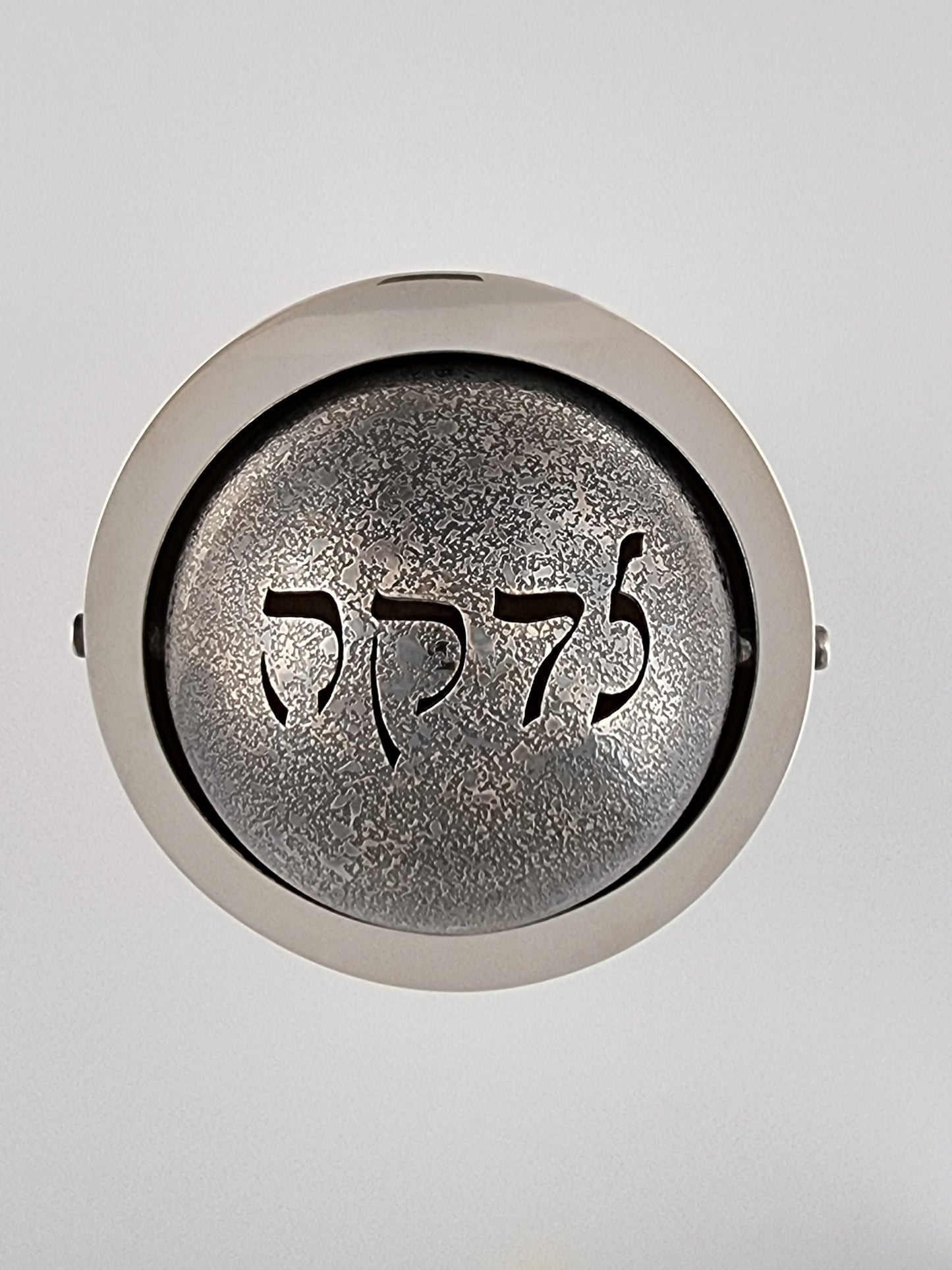 The word "Tzedakah" in Rashi script is pierced through the etched silver ball.