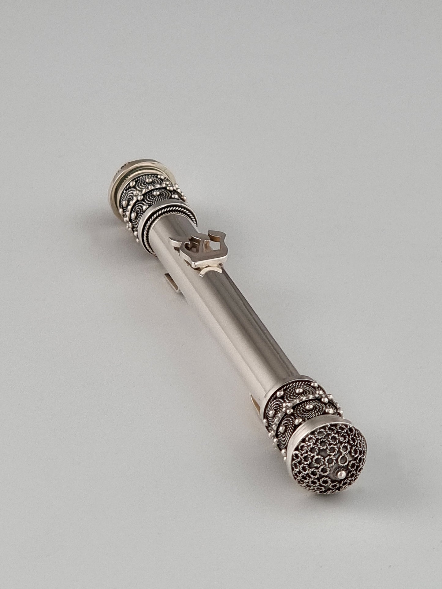 Fine filigree Mezuzah laying diagonally.