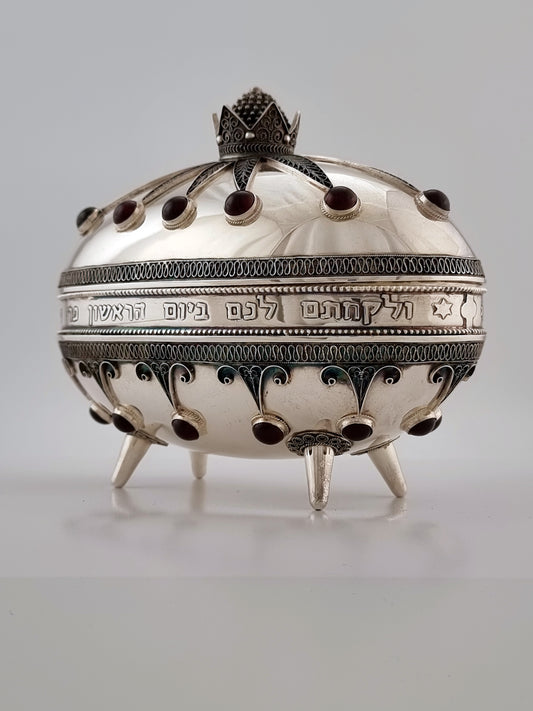 Isaiah Etrog Box. This signature piece was designed in 1950. The oval container measures 5½” in height and 6” in length and is made with sterling silver, red garnets and turquoise stones.