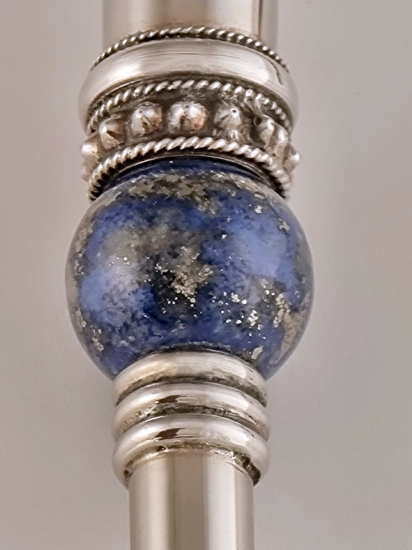 Amos Torah Pointer. This Torah pointer was designed in 1985. It is 8½” long and made of sterling silver and studded with three lapis lazuli stones.