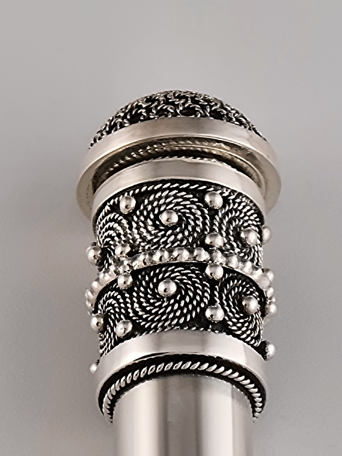 Intricate filigree elements at the top of this round silver Mezuzah