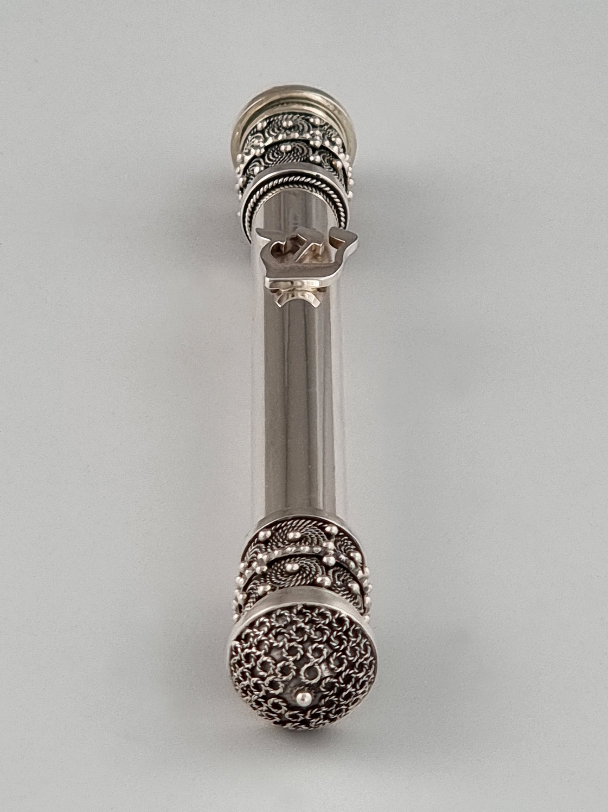 Sterling silver Mezuzah by Yaacov and Boaz Yemini. Both ends are heavily detailed and the center is round and smooth.