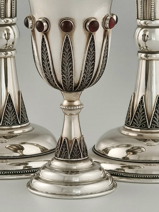 Jacob Kiddush Set. It is made of sterling silver, gold-plated silver and garnet stones; ten on the cup and seven on each candlestick. The cup is 5½" high and the candlesticks are 10” high.